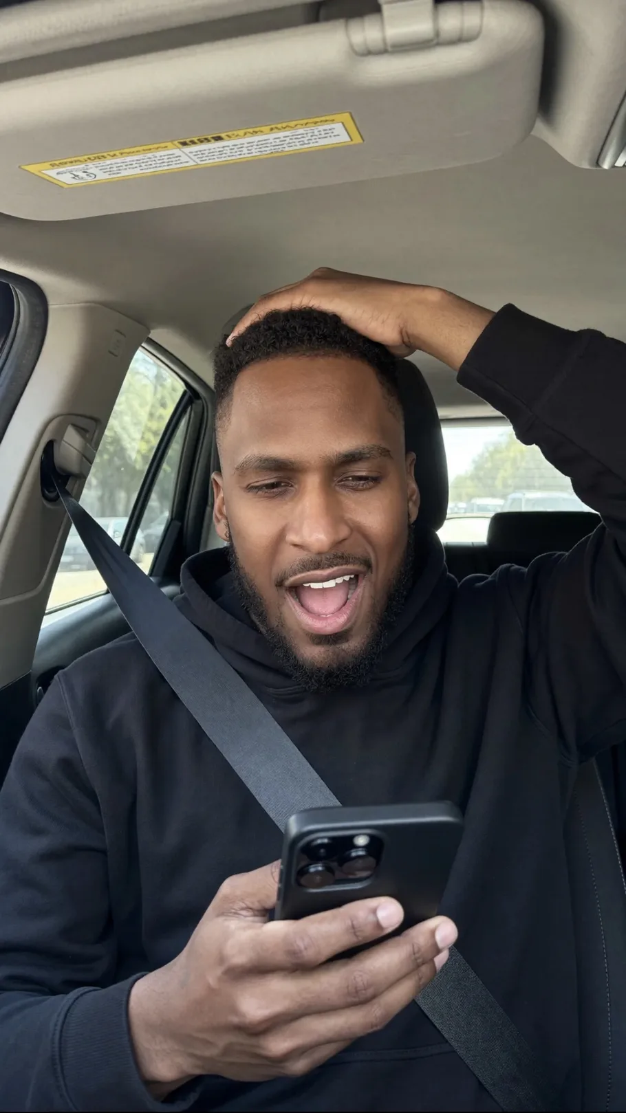 King The Kemist in the passenger seat of a car, hand on his head, reacting to something on his phone